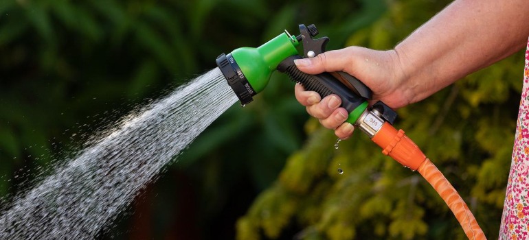 A person holding a garden hose that's essential for artificial grass maintenance Las Vegas.