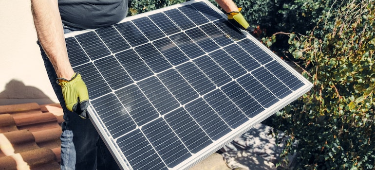 A person holding solar panel while standing on the roof